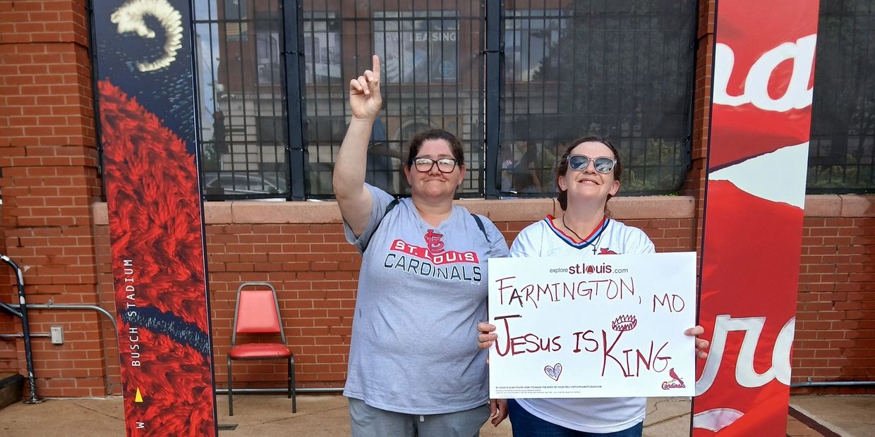 Two St. Louis Cardinals fans holding a sign that says "Farmington, MO Jesus is King."