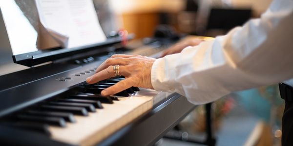 A person playing a digital piano with sheet music in the background.