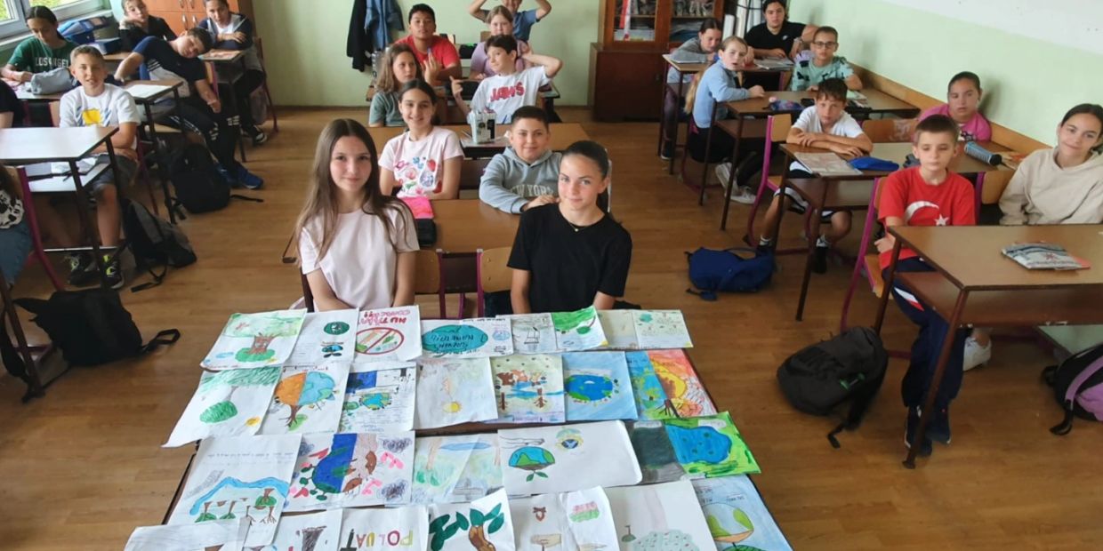 Students in a classroom displaying environmental drawings on their desks.