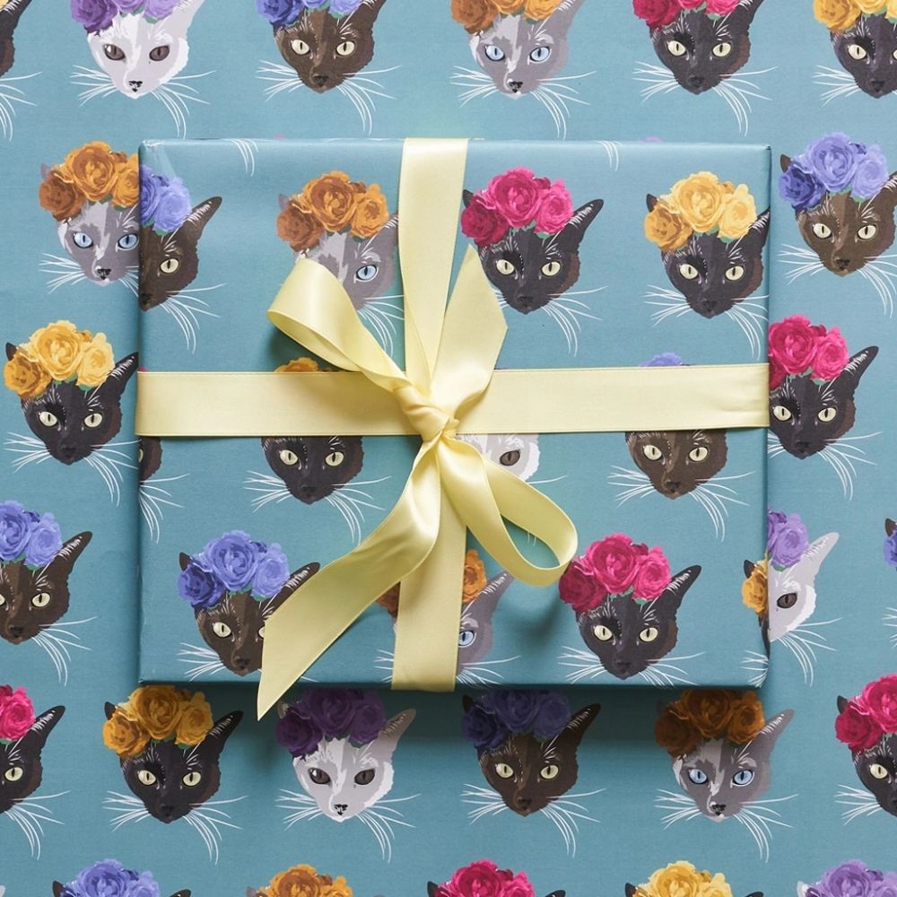 Cat wrapping paper arid a box with a yellow bow.