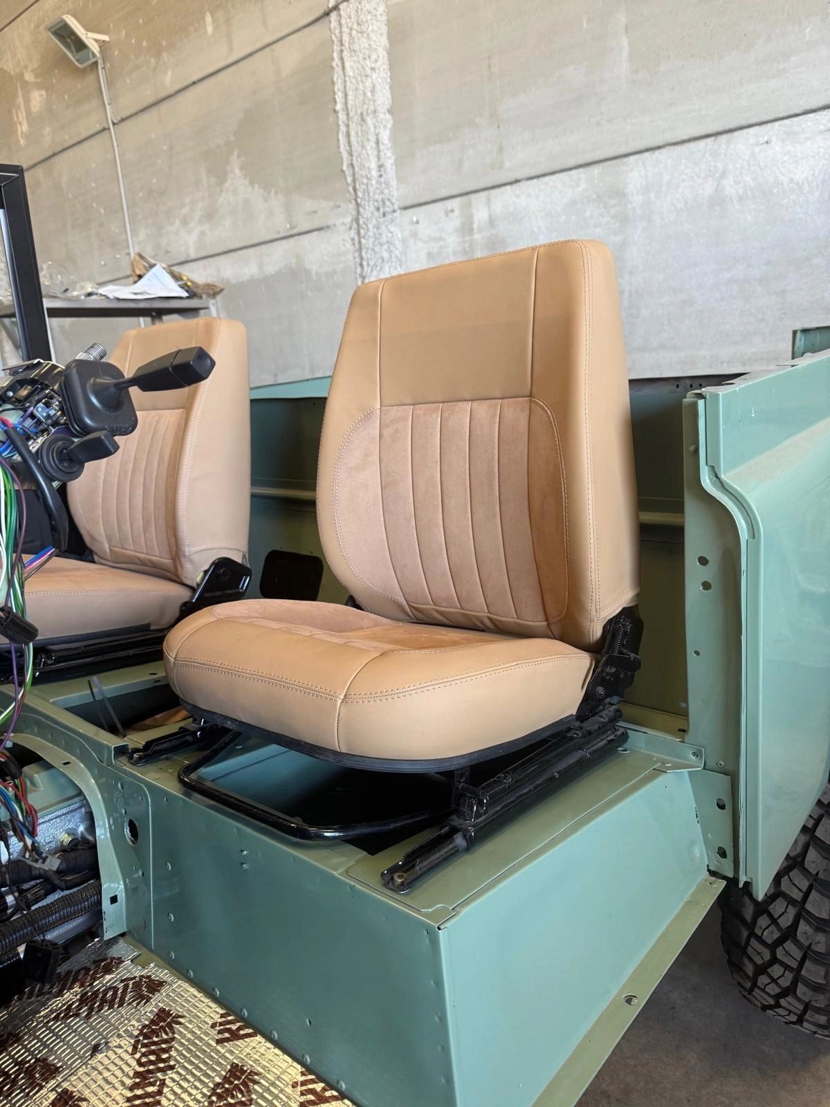 Tan leather car seats installed in a partially assembled green vehicle frame.