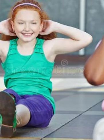 Smiling girl exercising indoors, wearing a green top and purple shorts.
