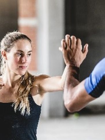 Woman practicing self-defense with a partner indoors.