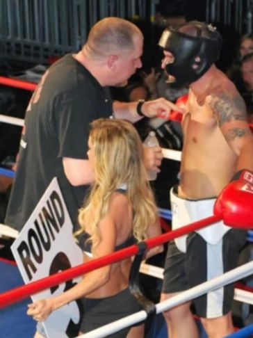 Boxer receives coaching while a ring girl holds a round sign in the boxing ring.