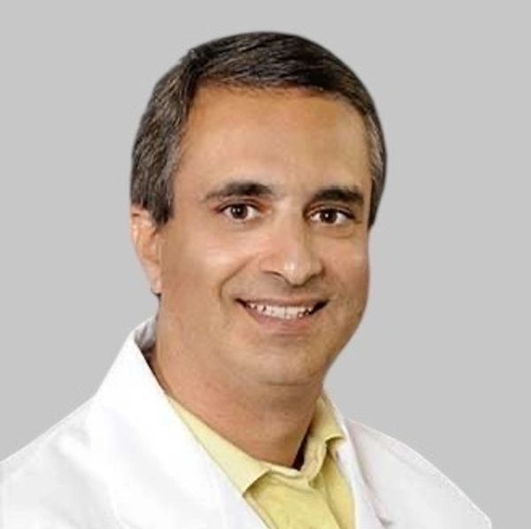 Smiling man in white coat with yellow shirt.