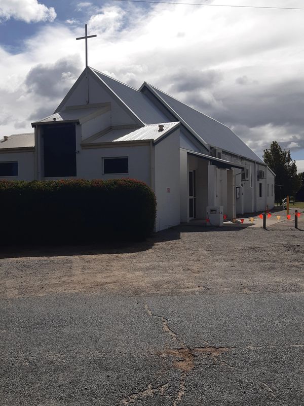 A white church building with a cross on the roof under a cloudy sky.