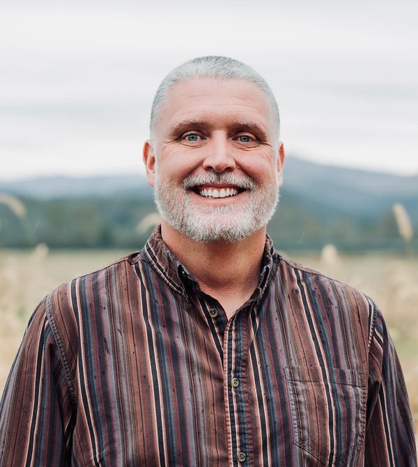 Smiling middle-aged man with gray hair and beard outdoors.