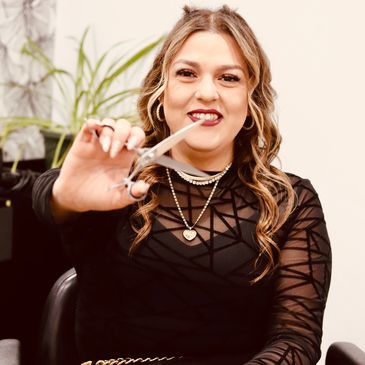Smiling hairstylist holding scissors towards the camera.
