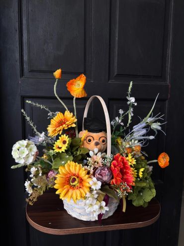 Basket of vibrant flowers with a doll inside.