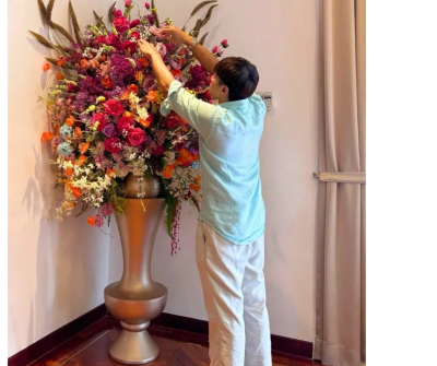Person arranging flowers in a large vase indoors.