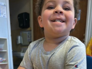 A smiling young child in a grey Champion t-shirt.
