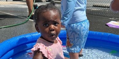 A young child playing in a small blue inflatable pool outdoors.