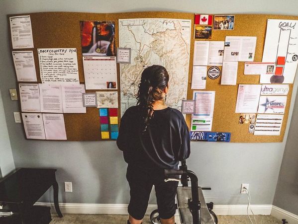 Cara facing a vision board in her home, with a map of grand canyon, notes, lists, and quotes on it
