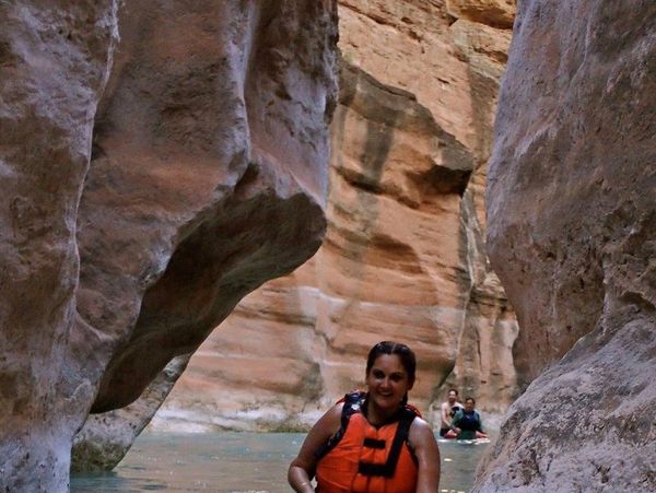 Cara is sitting on a paddle board floating in between a narrow pale pink wall in the canyon. 
