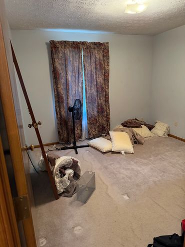 Empty bedroom with scattered pillows and a detached door.