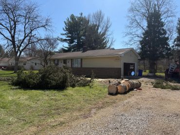 A suburban house with fallen tree logs and branches in the yard.