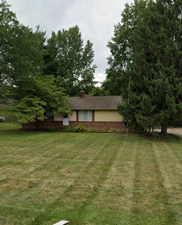 Small single-story house with a large front yard and tall trees.