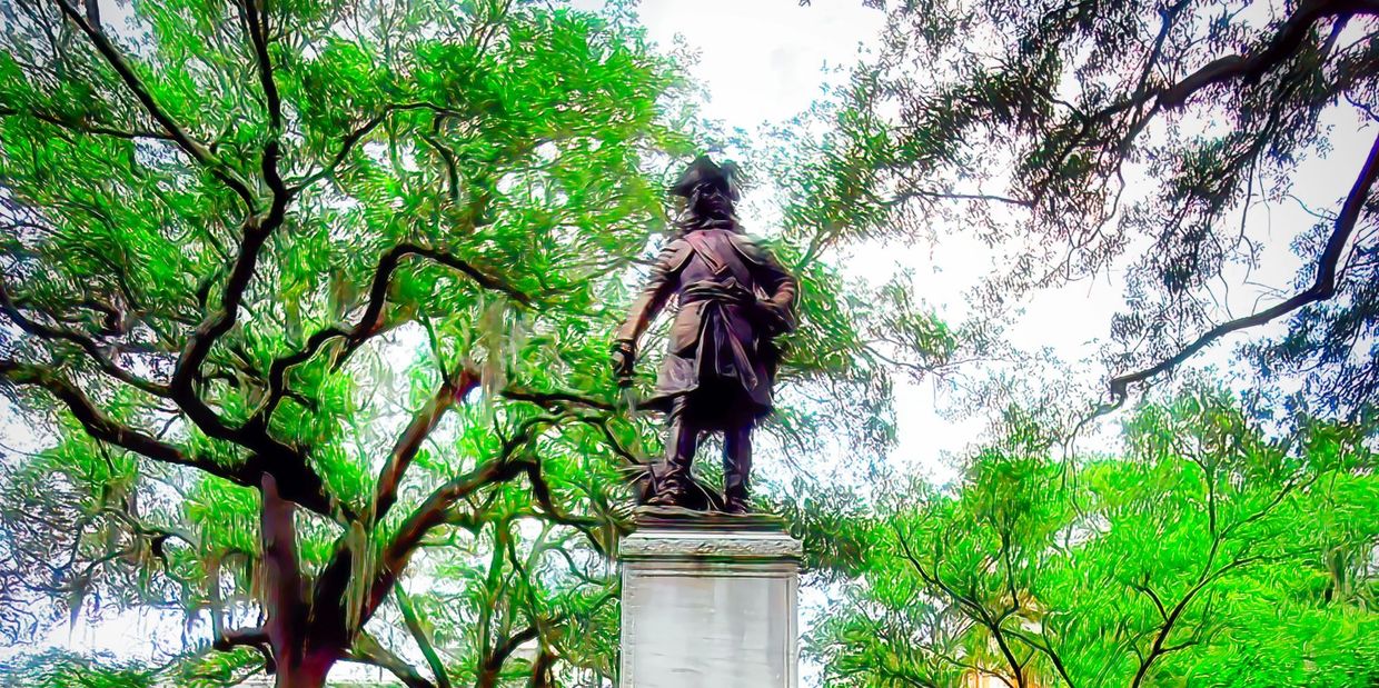 Statue of a historical figure surrounded by lush green trees in a park.