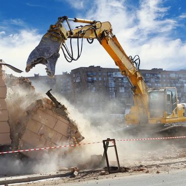 Yellow excavator demolishing a building amid dust and rubble in an urban area.