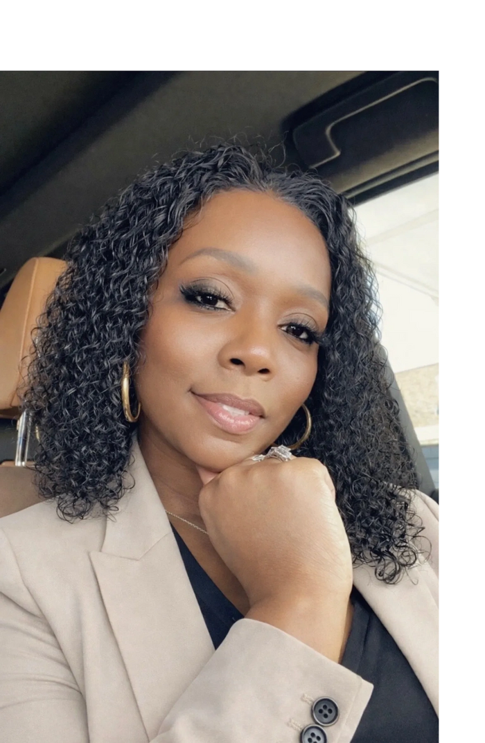 Confident woman with curly hair and hoop earrings, dressed in a beige blazer.