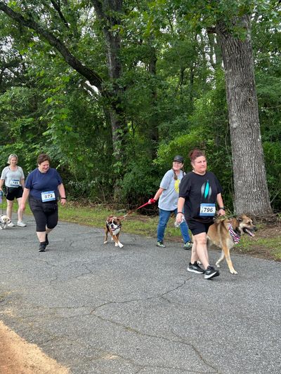 A group of participants walk along a paved, tree-lined trail during a community event. Several women