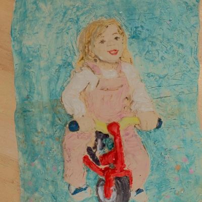 Sculptural relief made from kiln-fired clay of a small child riding a red bicycle.
