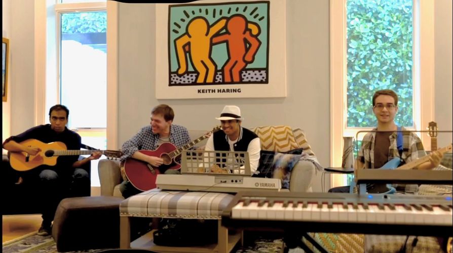 Four young men playing guitars and keyboard in a cozy living room with Keith Haring artwork.