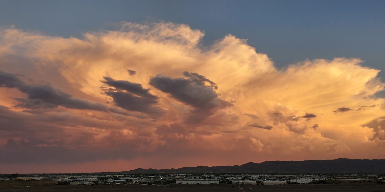 Dramatic sunset clouds glowing over a cityscape with mountains in the background.