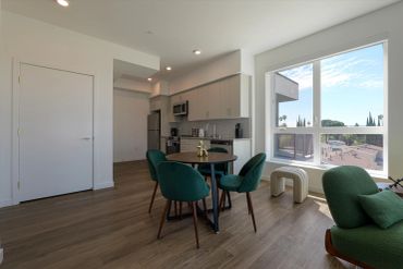 Modern kitchen and dining area with large window and green chairs.