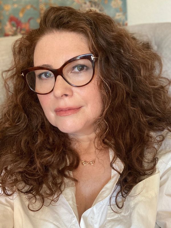 Susanna Brisk in cat-eye glasses, red hair, wearing a white shirt. 