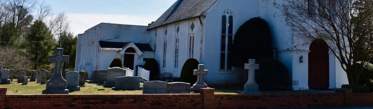 White church with a graveyard and tombstones in front under a clear sky.