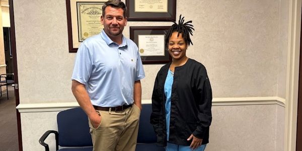 Two people standing in an office with framed certificates on the wall.