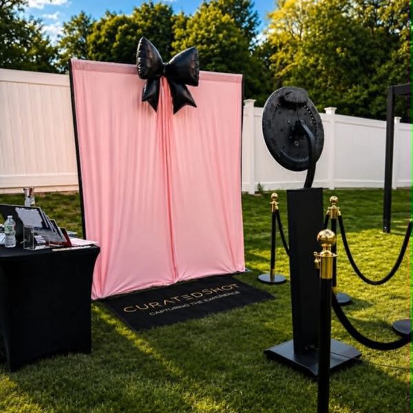 Outdoor photo booth setup with pink backdrop and black bow.