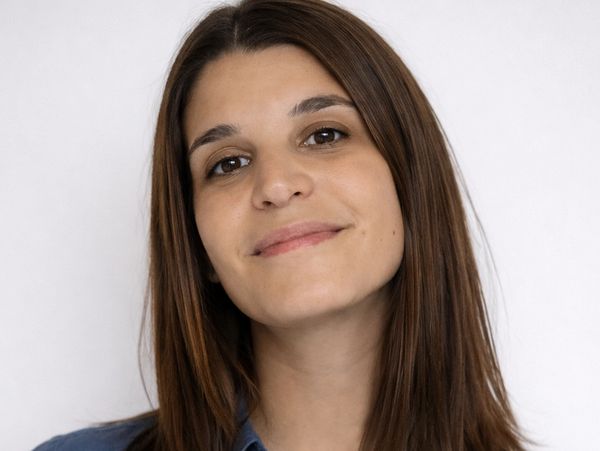 Young woman with straight brown hair wearing a blue shirt, smiling gently.