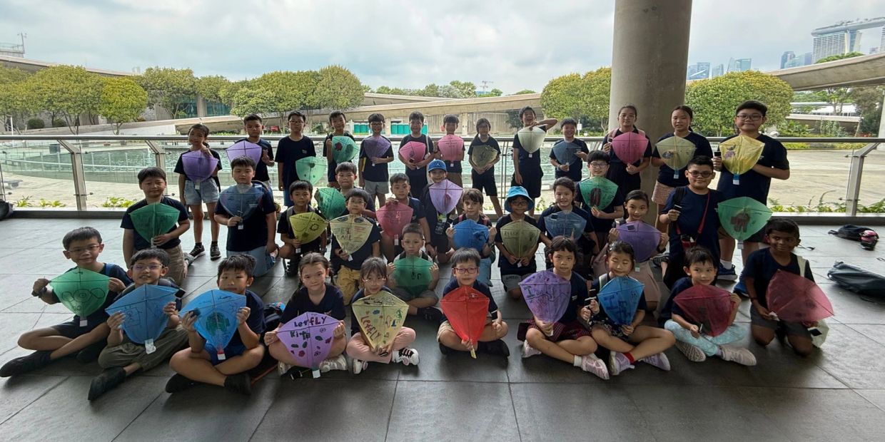 A large group of children holding colorful handmade kites outdoors.