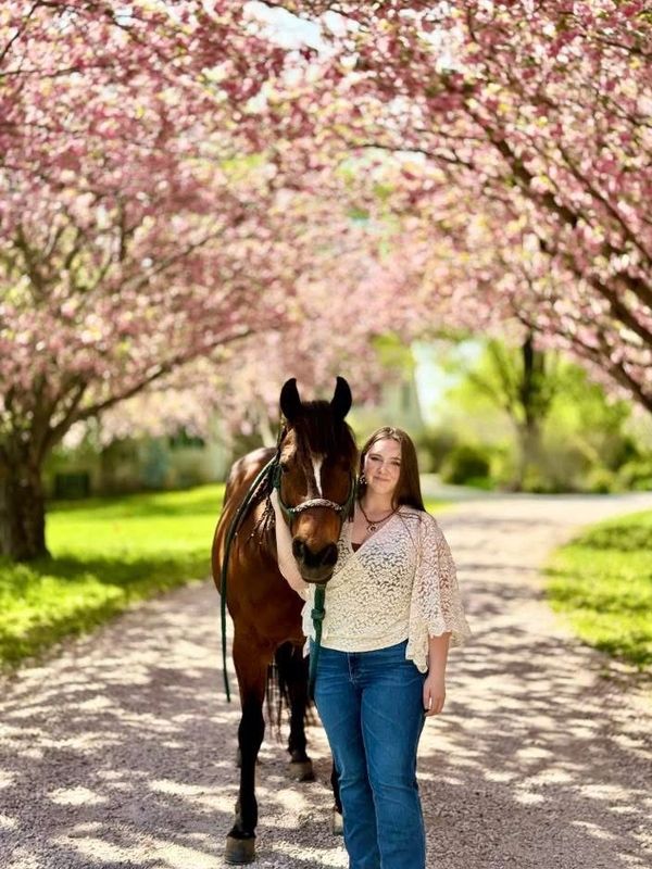 Young woman standing beside a brown horse under blooming cherry trees.
