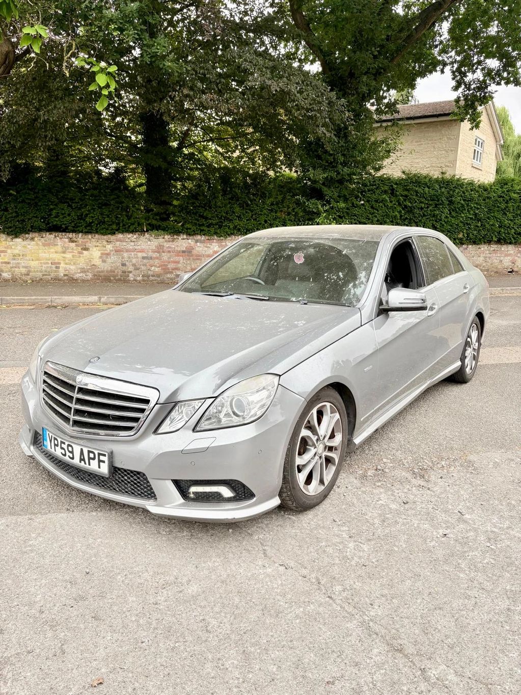 Silver Mercedes-Benz parked on a street near greenery.
