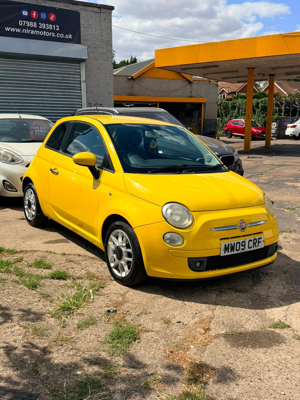 Yellow Fiat 500 parked at a car dealership.