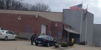 People outside a post office building with American and state flags.