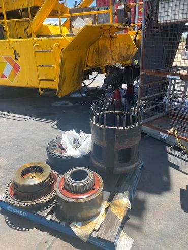 Heavy machinery parts on a pallet near a yellow crane.