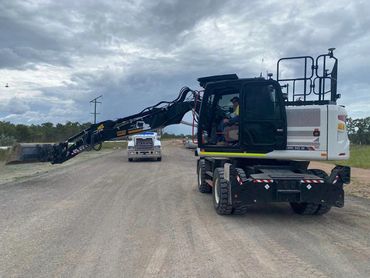 Large excavator on a dirt road with a truck in background.