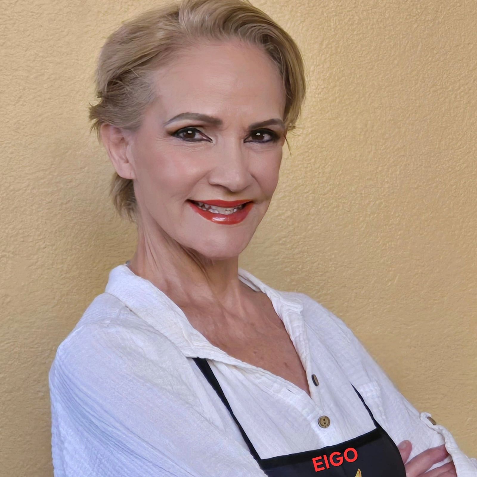 Smiling woman with short blonde hair wearing a white shirt and black apron.