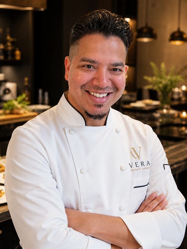 Smiling chef in white uniform stands confidently in professional kitchen.