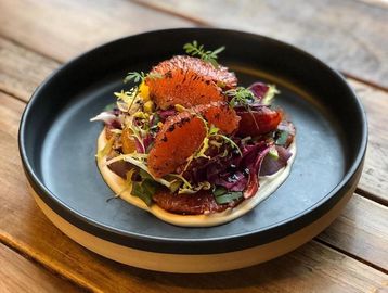 Gourmet dish with citrus segments and fresh herbs on a black plate.
