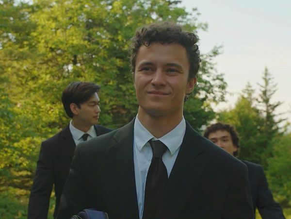 Three young men in suits outdoors with a forest background.