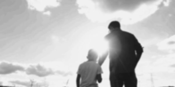 Silhouettes of a man and child against a bright sky at sunset.