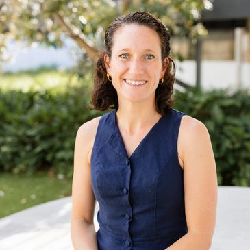 Smiling woman in a navy blue sleeveless dress outdoors.