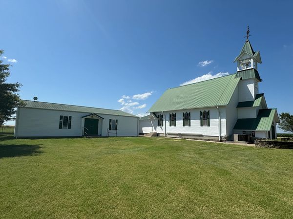 White church and building with green roofs on a sunny day.