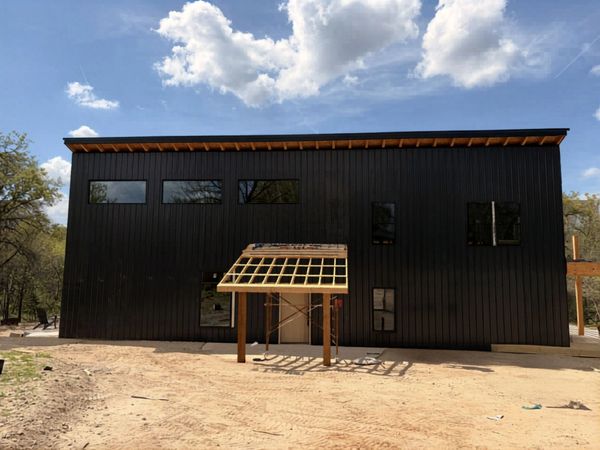 Modern black building under construction with wooden framework for entrance.