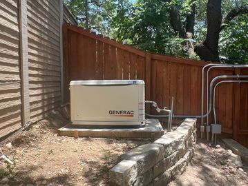 Generac generator installed on a concrete platform beside a wooden fence.